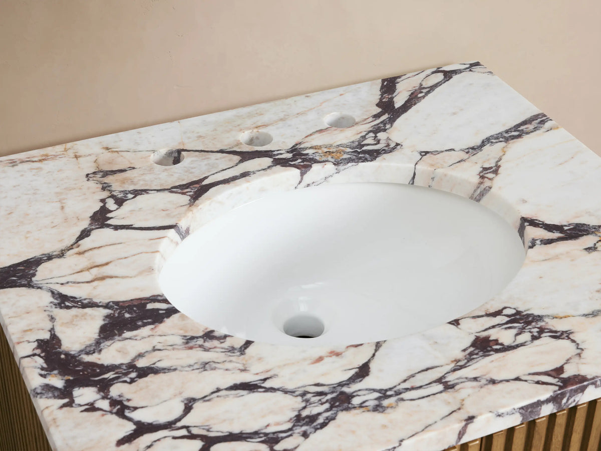 Close-up of Finnley Powder Vanity with white oval sink, Calacatta Viola marble top, bronze faucet, flowers, soap, and salts.