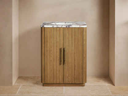 Finnley Powder Vanity: Light fluted wood cabinet, white marble top with brass faucet, soap dispenser, and small vase.