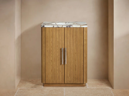 Finnley Powder Vanity: Fluted oak wood cabinet, white Carrara marble top, chrome faucet & handles. Beige wall, tiled floor.