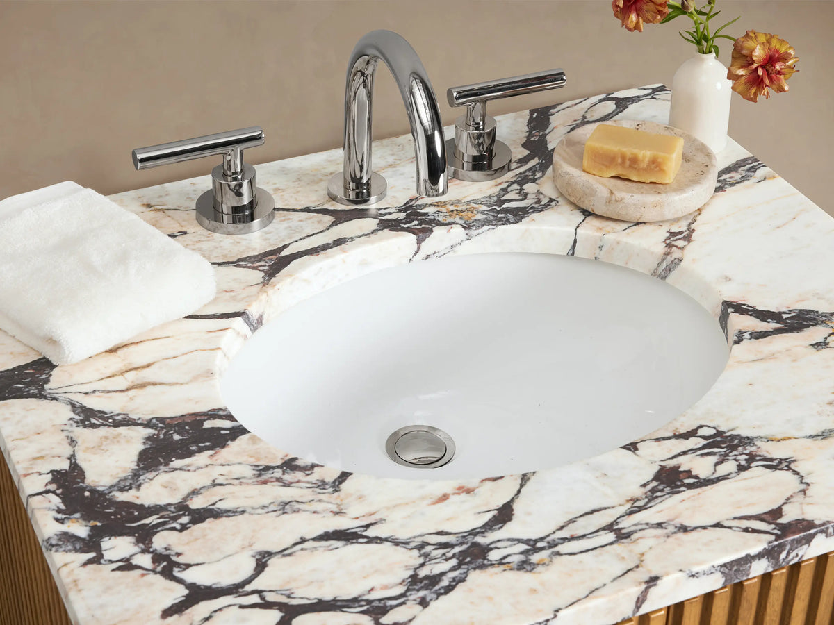 Finnley Powder Vanity: light oak wood, reeded doors, silver handles, white marble top with sink, set in a beige room.