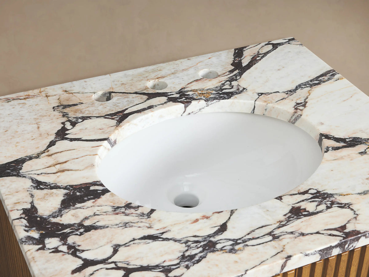 Close-up of Finnley Powder Vanity with white oval sink, chrome faucet, striking cream/black marble top, white towel, soap, and flowers.