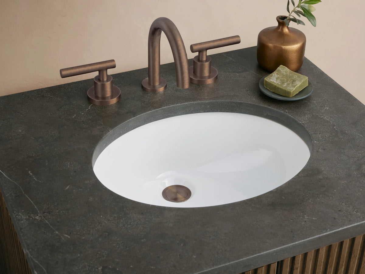 Finnley Powder Vanity, dark fluted wood cabinet with dark stone top, oval sink, & dark faucet against a warm beige background.