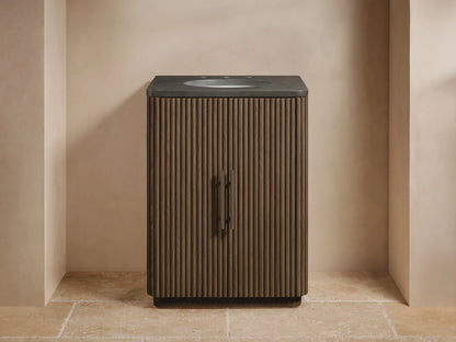 Finnley Powder Vanity's fluted dark wood door slightly open, revealing an antique bronze handle, folded towels & toiletries inside.