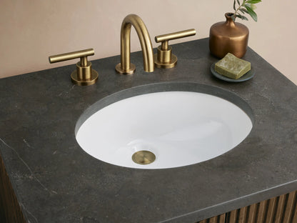 Finnley Powder Vanity: dark ribbed wood cabinet, brass handles, dark stone top, and oval sink, in a light room.