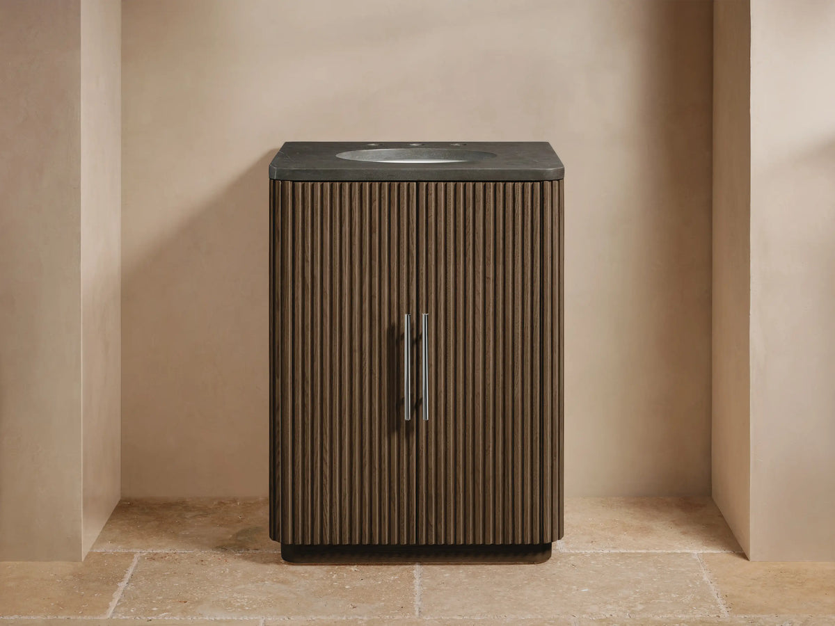 Finnley Powder Vanity, dark fluted wood cabinet with two doors, dark stone top, white oval sink, chrome faucet & handles.