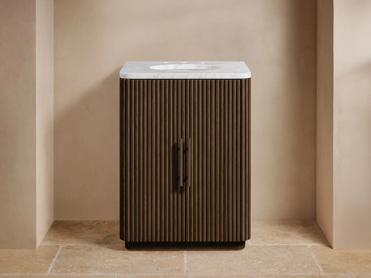 Front view of Finnley Powder Vanity with fluted dark wood, white marble top, bronzed faucet & handles, and soap/bottle.