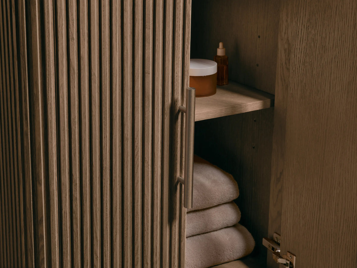 Close-up of Finnley Powder Vanity: white Carrara marble top with oval ceramic undermount sink & 3 faucet holes. Fluted dark wood base.