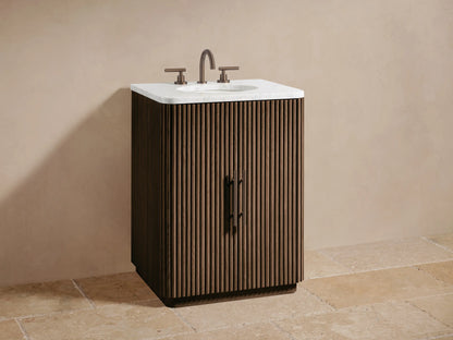 Finnley Powder Vanity cabinet, fluted light wood door ajar with brushed nickel handle, revealing cosmetics on shelf, stacked towels.