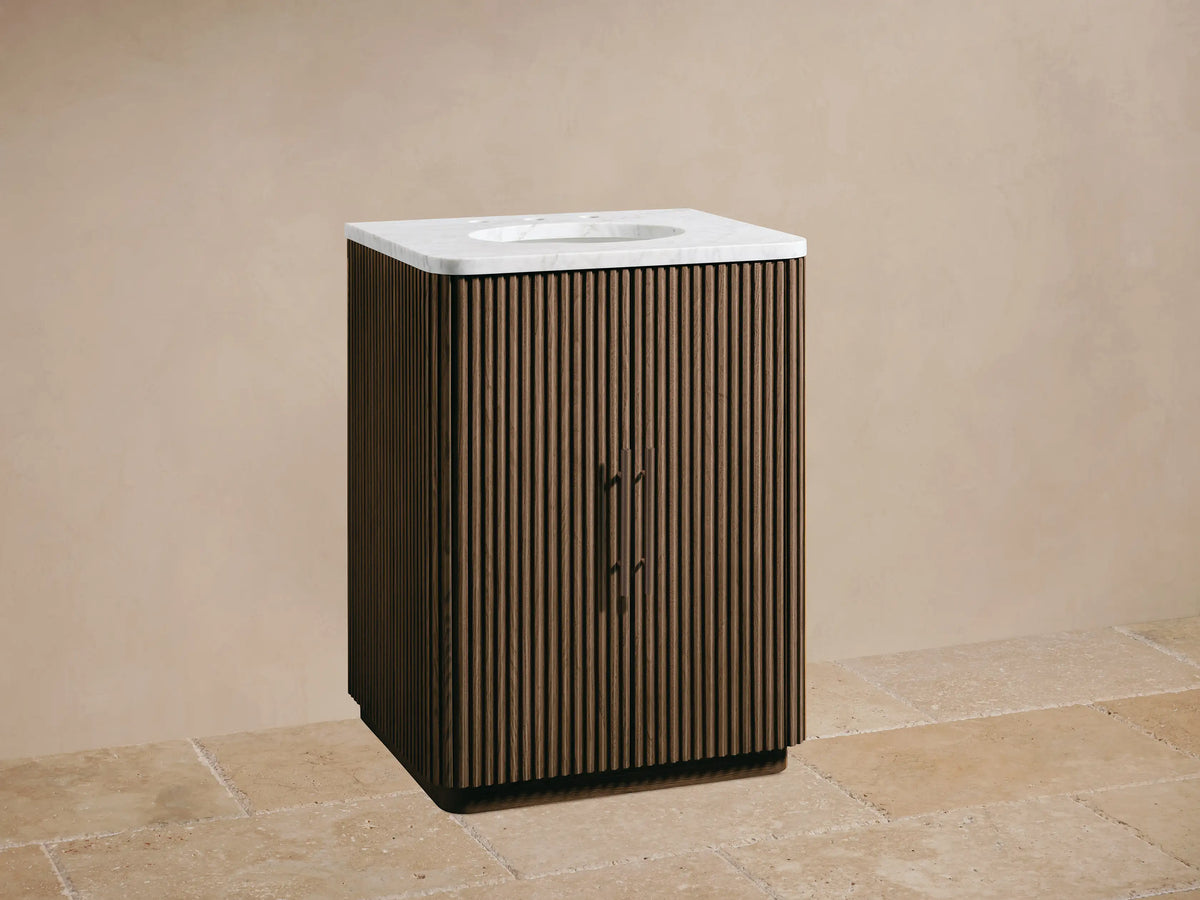 Fluted dark oak Finnley Powder Vanity with white marble top, oval sink, and dark faucet against a beige wall.