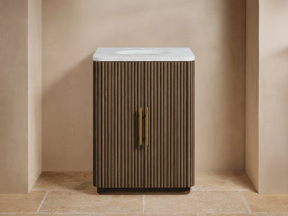 Finnley Powder Vanity. Brown fluted oak vanity, white marble top, gold faucet & two vertical brass handles, on stone tile.
