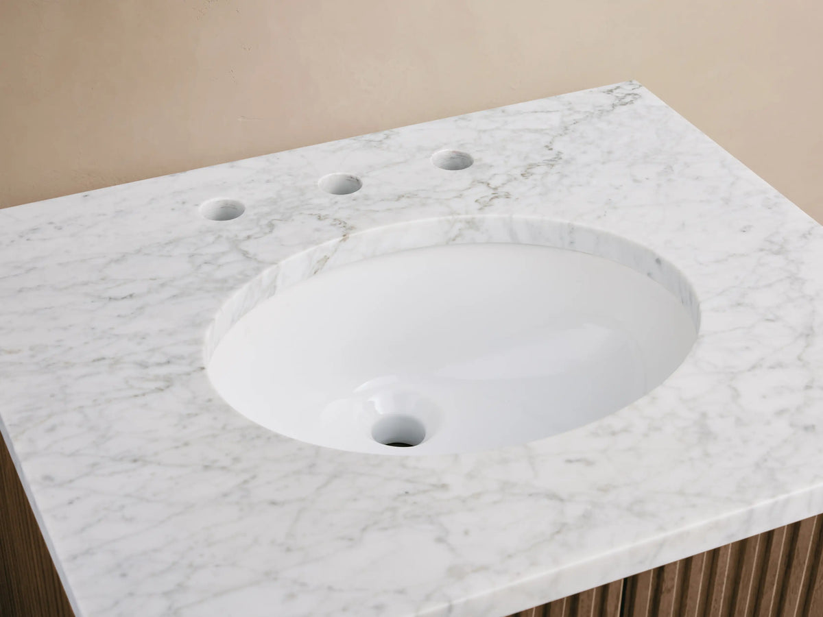 Close-up of Finnley Powder Vanity with white Carrara marble top, oval sink, brass faucet, amber bottle, and soap dish.