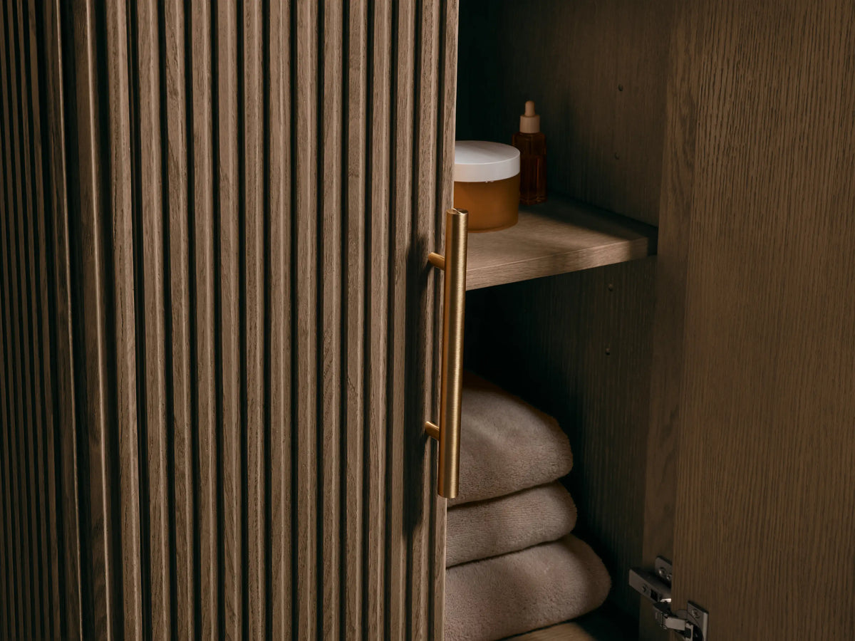 Close-up of Finnley Powder Vanity top. White oval sink in veined Carrara marble countertop with 3 faucet holes. Slatted wood base.