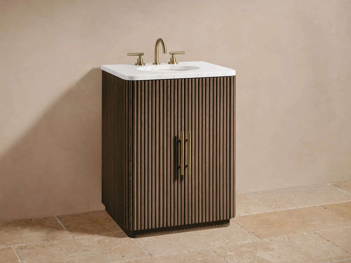 Close-up of Finnley Powder Vanity's open cabinet door with vertical fluting & brass pull, revealing shelf with toiletries & stacked towels.