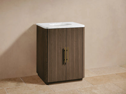 Finnley Powder Vanity: dark brown reeded wood, white marble top, oval sink, brass faucet/handles. Beige wall, tiled floor.