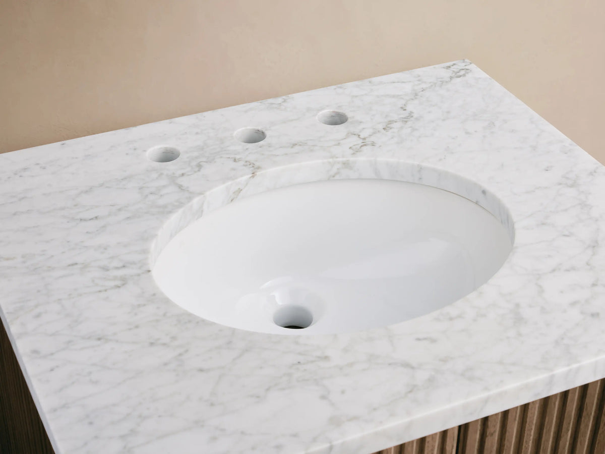 Finnley Powder Vanity: white oval sink, veined Carrara marble top, polished nickel faucet, ribbed vase, bar soap, beige towel.