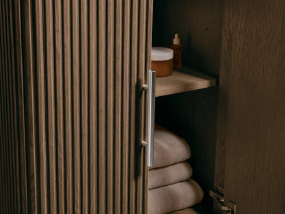 Close-up Finnley Powder Vanity. White oval ceramic sink in Carrara marble top with gray veining & faucet holes. Fluted wood base.