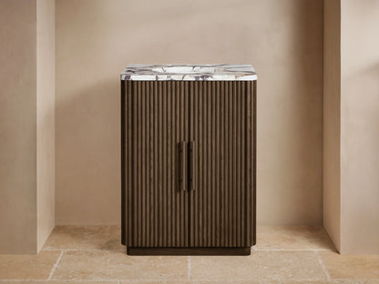 Finnley Powder Vanity: Dark reeded wood, white marble top, bronze faucet, vase, & soap dispenser in a beige room.