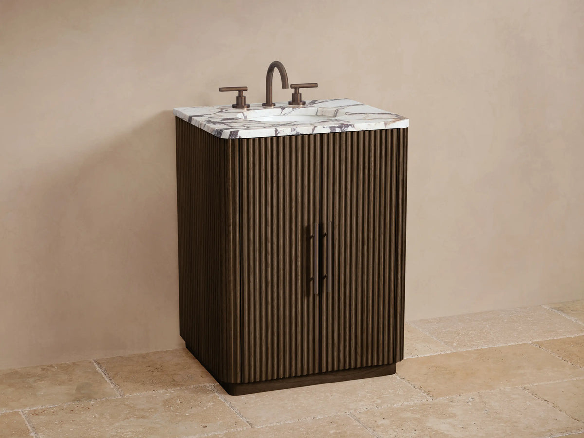 Finnley Powder Vanity's open cabinet door with reeded dark wood panel, revealing shelves with bottles and neatly stacked beige towels.