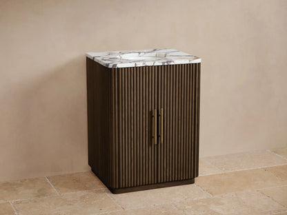 Finnley Powder Vanity: Dark brown fluted cabinet, white Carrara marble top with brass faucet, and two brass door pulls.
