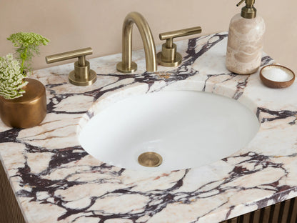 Fluted dark brown Finnley Powder Vanity with white Carrara marble top & sink, brass pulls, on beige tiled floor & wall.
