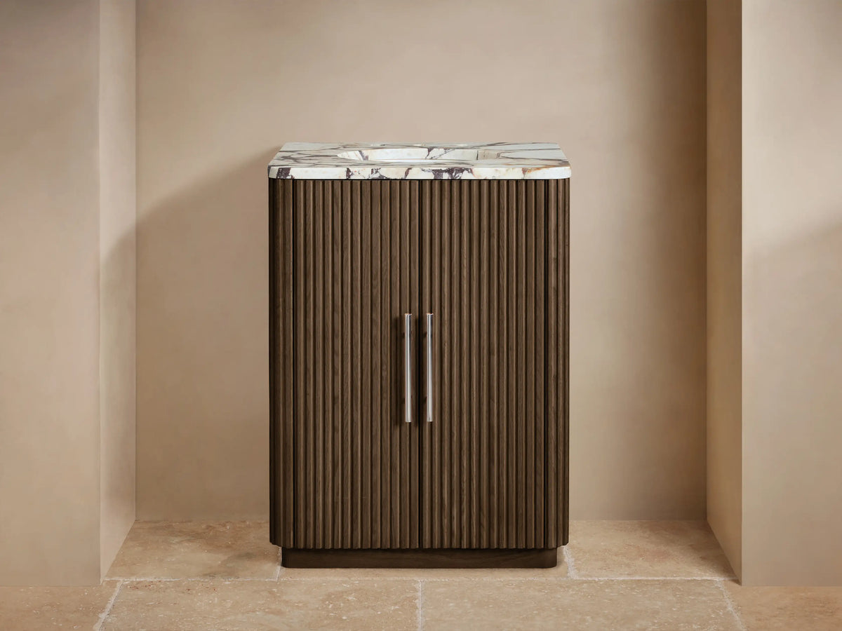 Finnley Powder Vanity with dark fluted wood cabinet, white marble top, polished nickel faucet, and a vase of flowers.