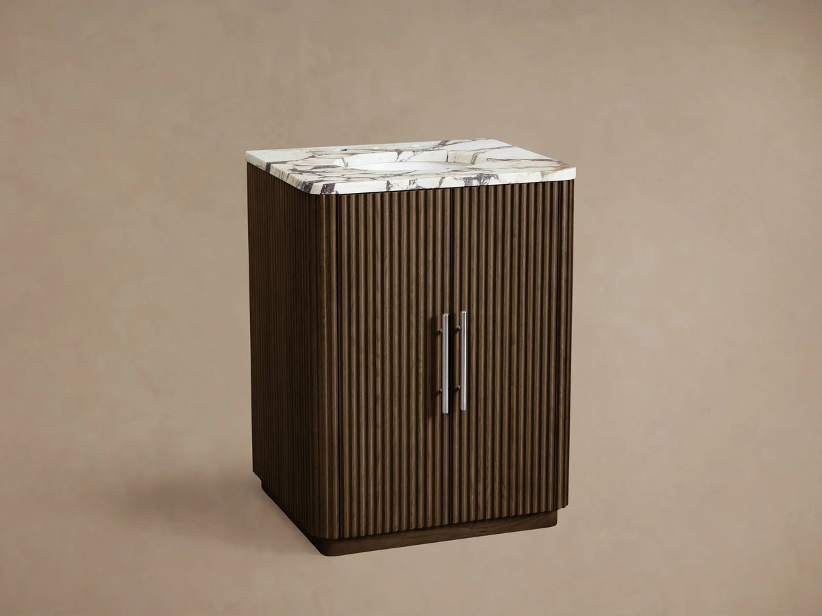 Finnley Powder Vanity: Dark brown ribbed wood vanity with a white marble top, silver handles, against a beige wall.