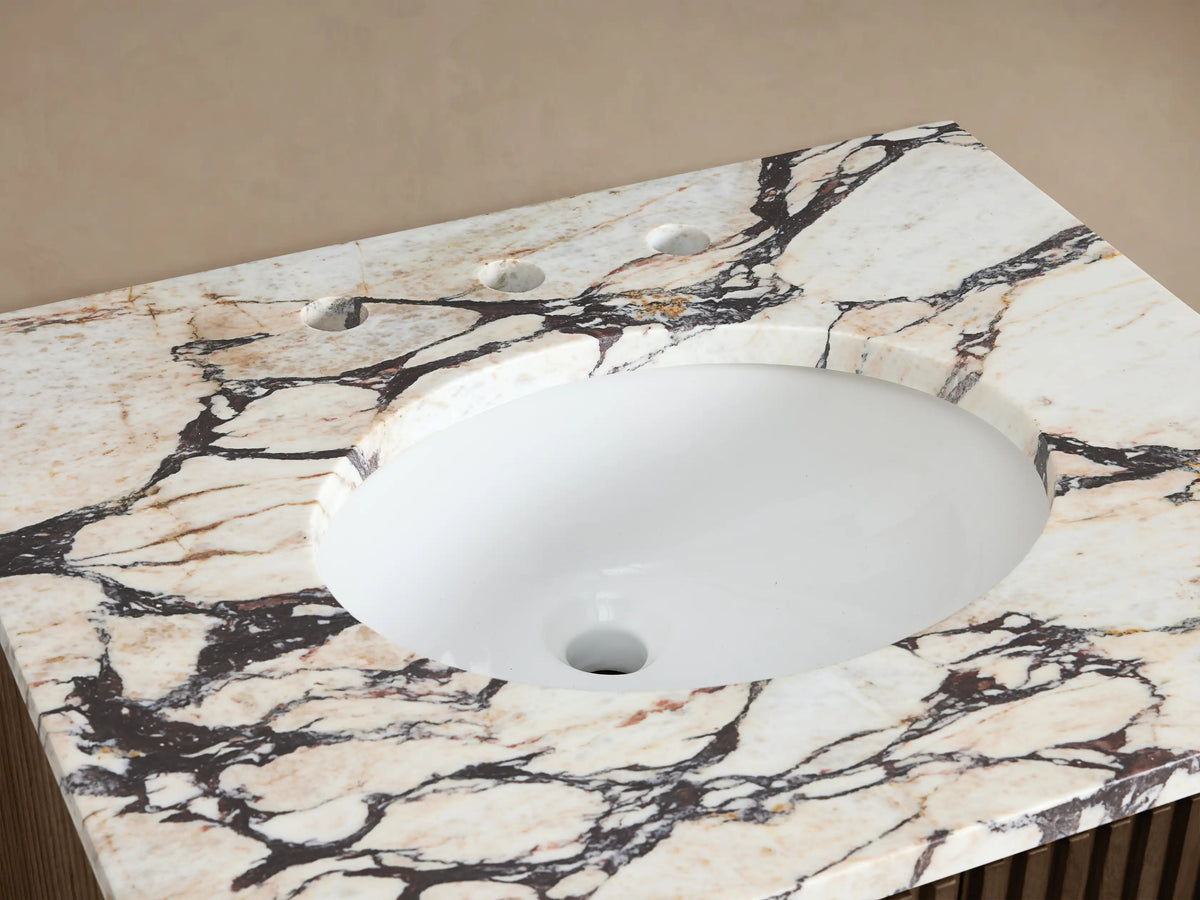 Finnley Powder Vanity with oval white sink, intricately veined stone countertop, polished chrome faucet, towel, soap & flowers.