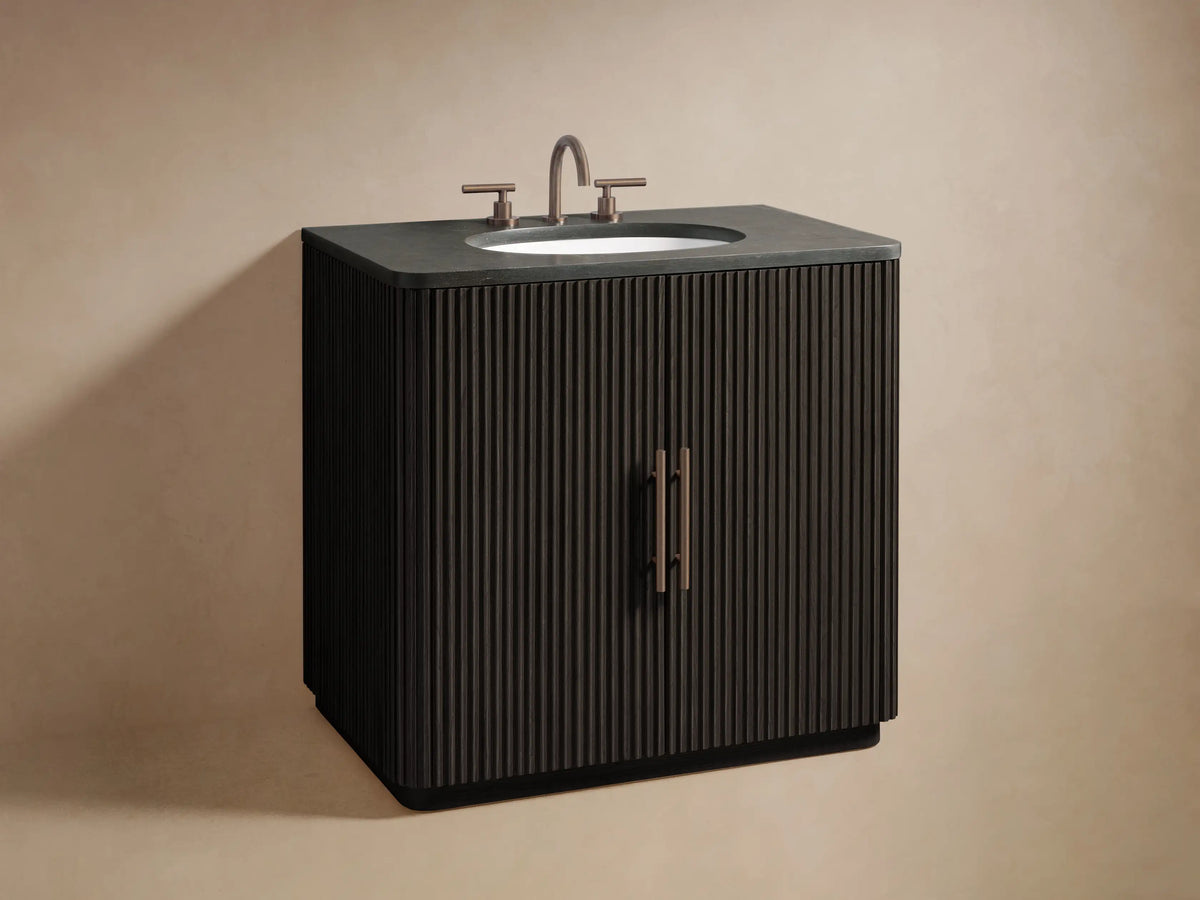 Finnley Single Vanity: dark reeded wood door, antique brass handles, slightly open, revealing folded towels and bath items.