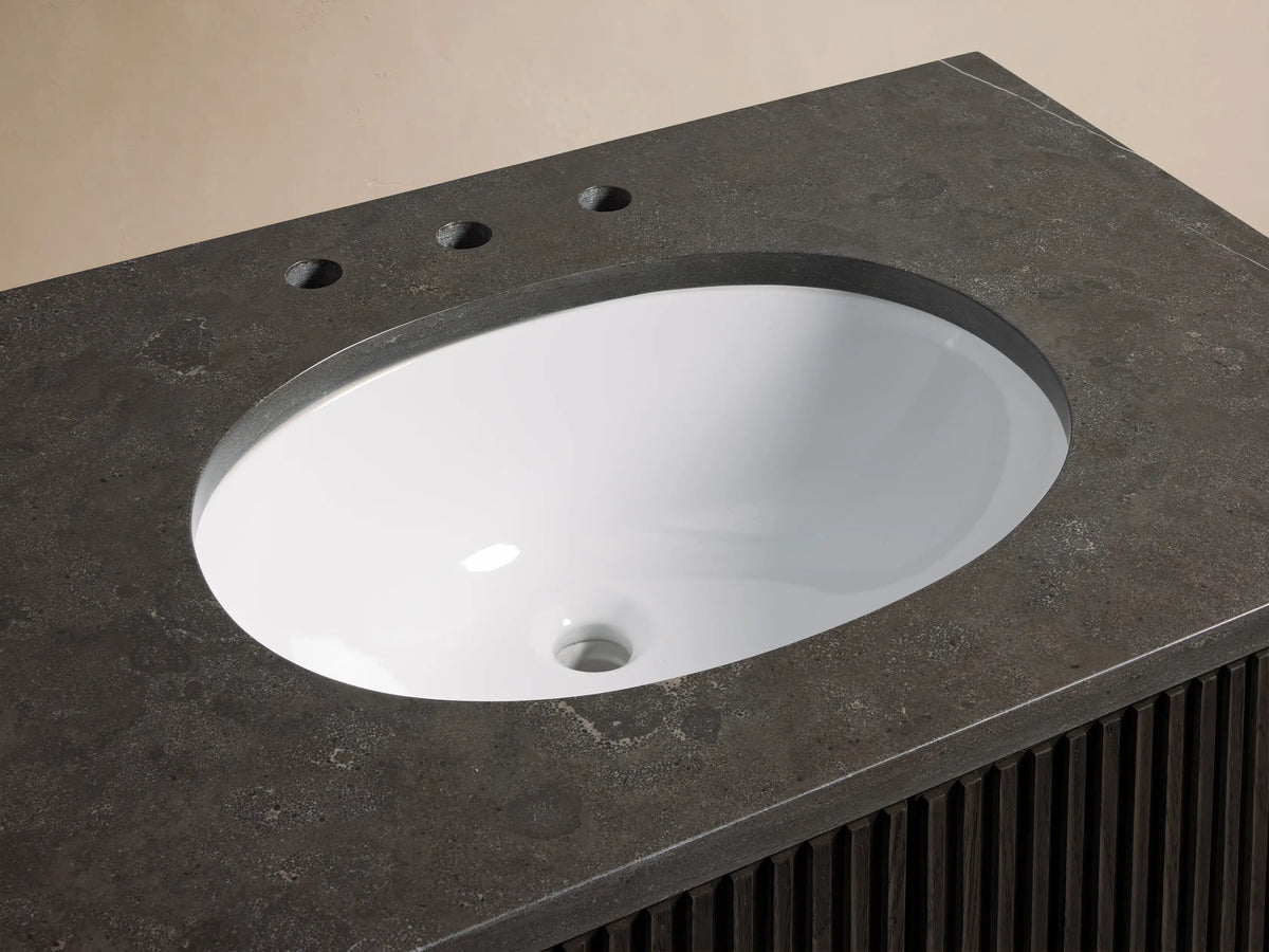 Finnley Single Vanity with dark stone top, oval white ceramic undermount sink, antique brass faucets, soap dish, and towel.