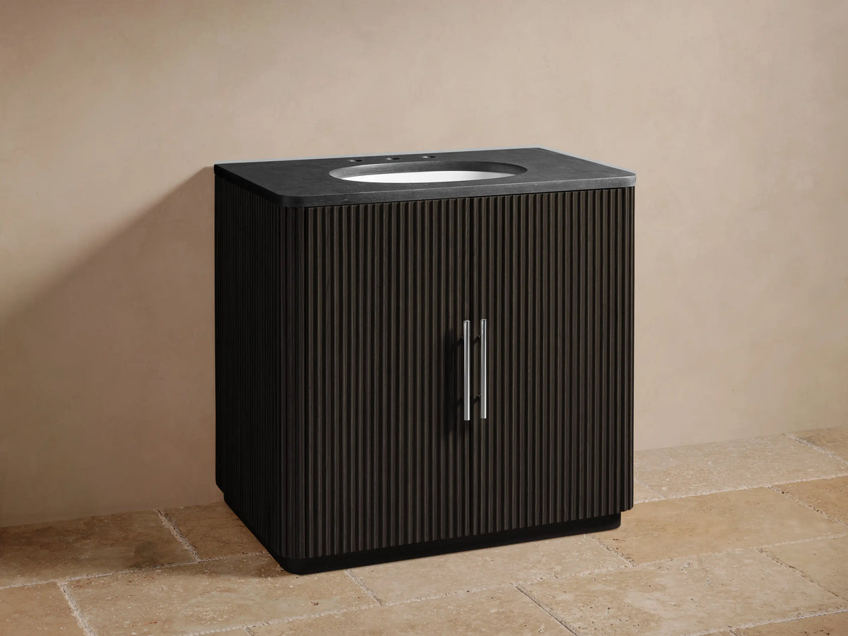 Open black cabinet of the Finnley Single Vanity, featuring ribbed texture, antique brass handle, and interior with towels and wooden tray.