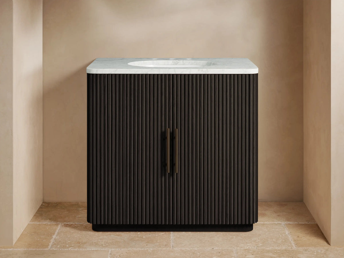 Finnley Single Vanity: dark brown fluted wood cabinet, white Carrara marble top, oval sink, bronze faucet, brass handles.