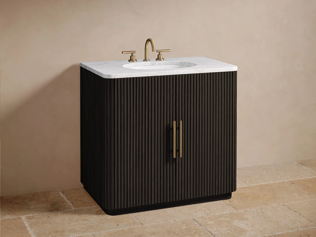 A partially open Finnley Single Vanity door shows a shelf with folded towels and grooming items. The door has a ribbed texture and brass handle.