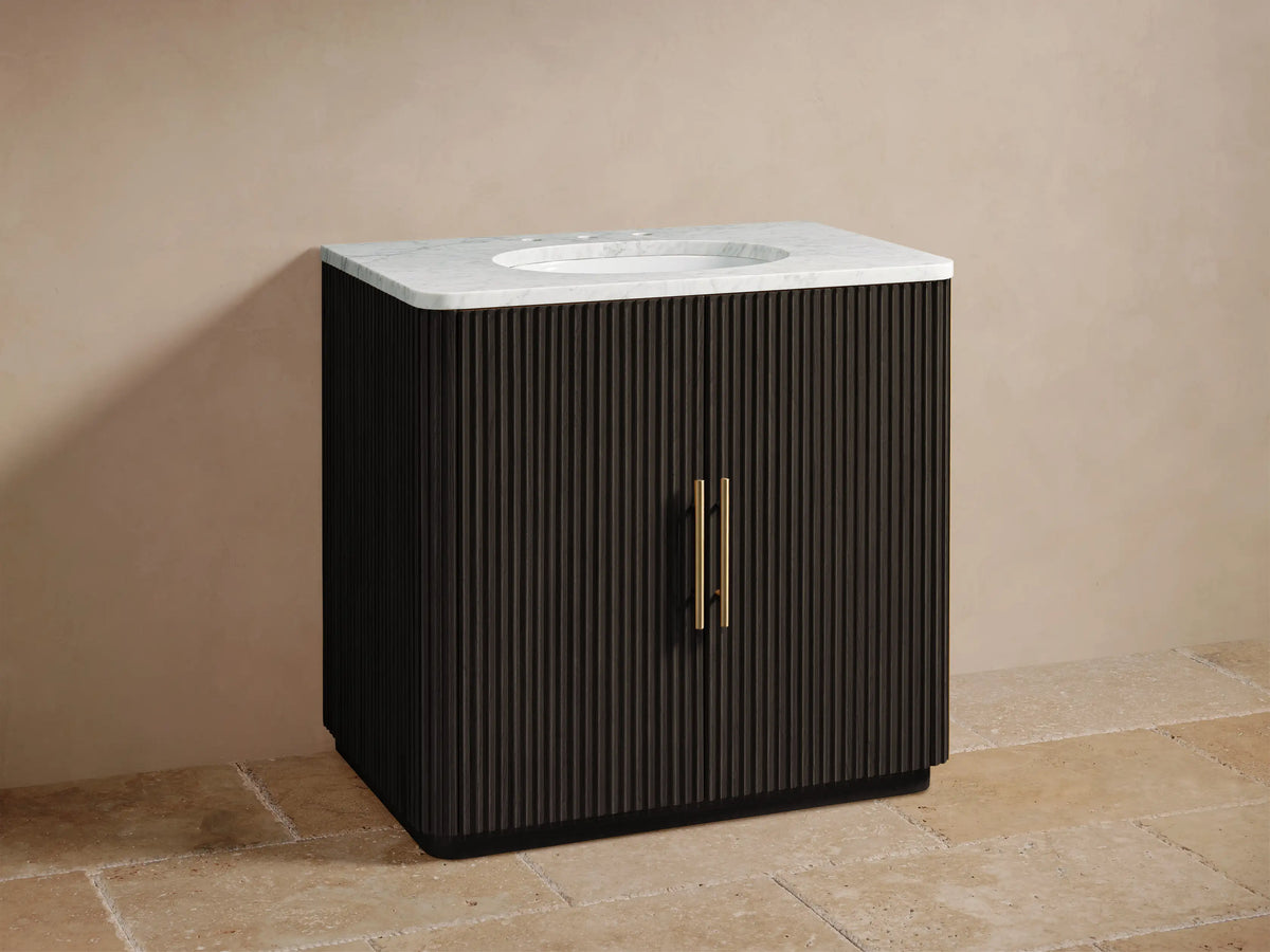 Finnley Single Vanity with dark oak wood finish, marble countertop, gold-tone faucet, and vertical groove design, placed on a stone floor.