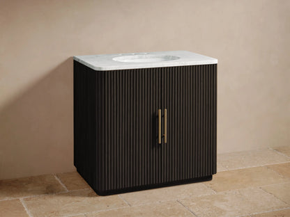 Finnley Single Vanity with dark oak wood finish, marble countertop, gold-tone faucet, and vertical groove design, placed on a stone floor.