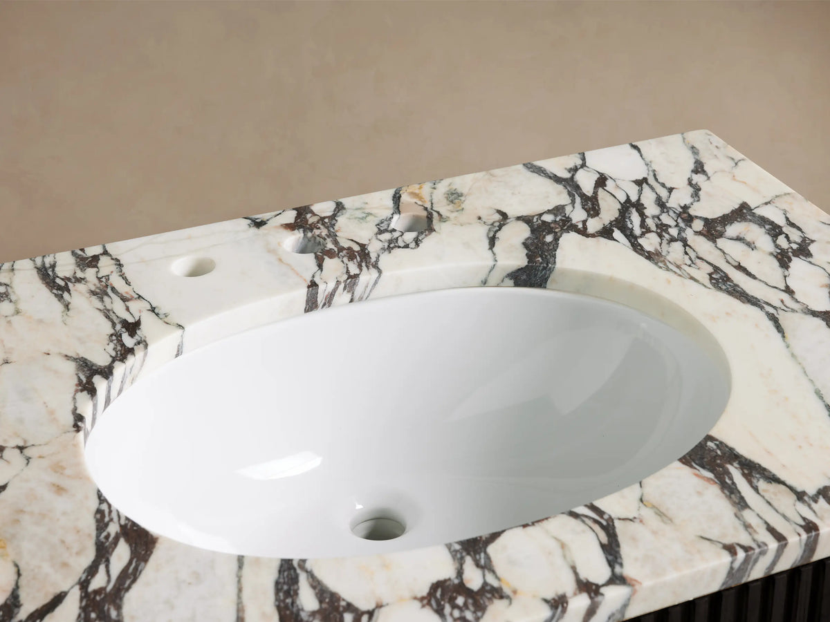 Finnley Single Vanity: White oval undermount sink, bronze faucet, and stone soap dispenser on dramatic veined marble countertop.
