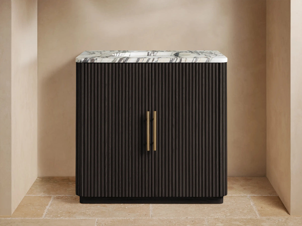 Finnley Single Vanity with a dark fluted cabinet, white veined marble top, brass faucet & handles in a neutral room.