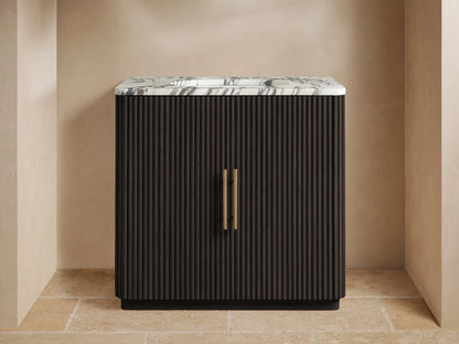 Finnley Single Vanity with a dark fluted cabinet, white veined marble top, brass faucet & handles in a neutral room.