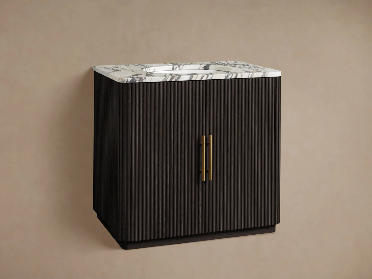 Finnley Single Vanity: dark brown ribbed cabinet, white marble top with integrated sink, gold faucet & handles, against a beige wall.