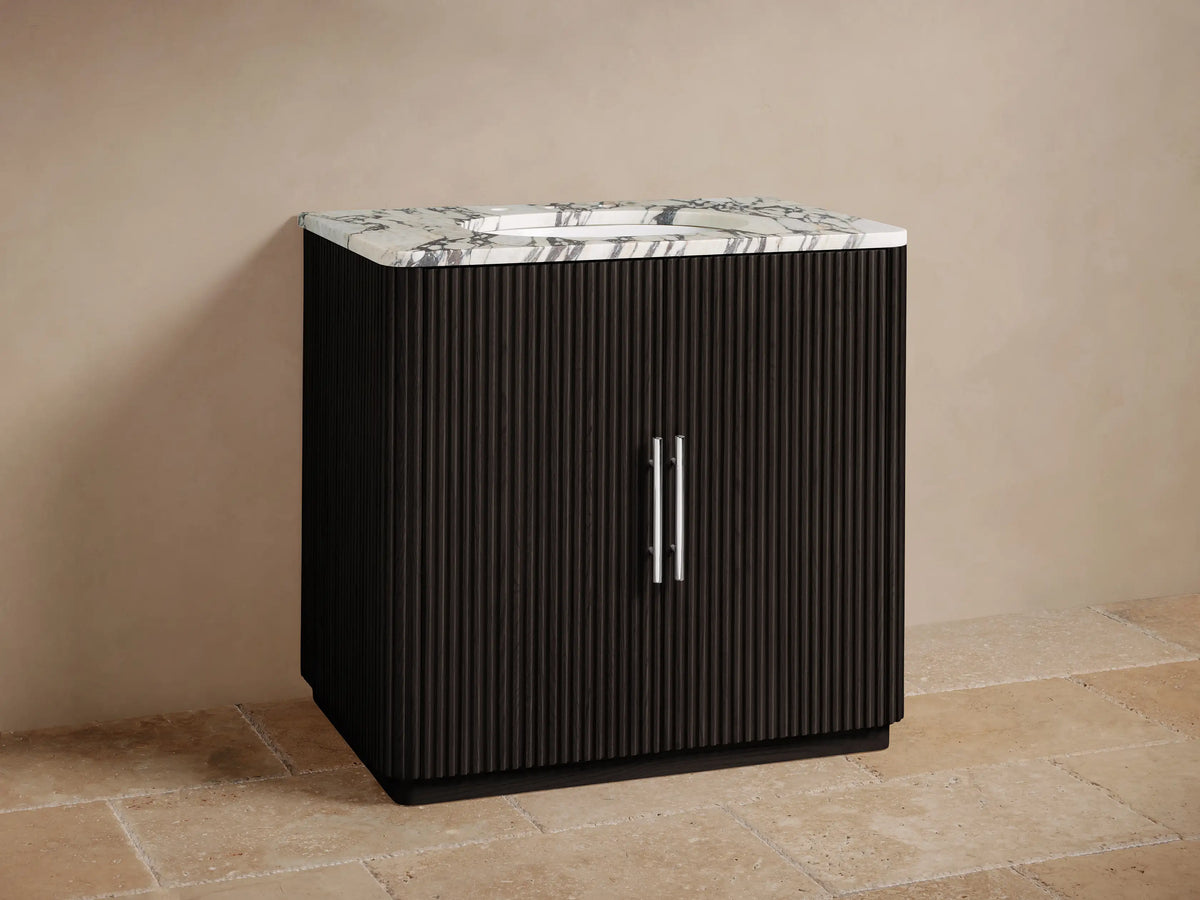 Finnley Single Vanity: black fluted cabinet, white marble top with chrome faucet & vertical pulls, against beige wall.