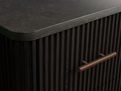 Front view of a dark, ribbed Finnley Short Bath Cabinet featuring a dark stone top and three drawers with antique bronze pull handles.