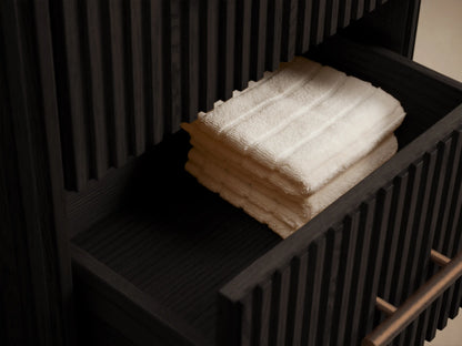 Finnley Short Bath Cabinet: Angled close-up of dark fluted wood, dark honed stone top, and cylindrical bronze handle.