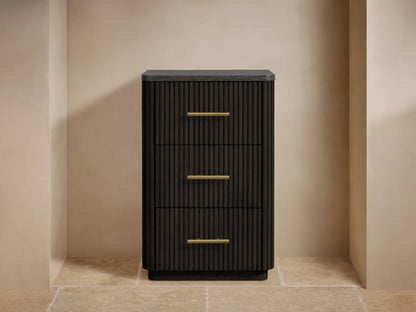 Finnley Short Bath Cabinet, dark fluted wood with 3 drawers, brass pulls, & dark stone top. Towels & vase on top in a beige room.