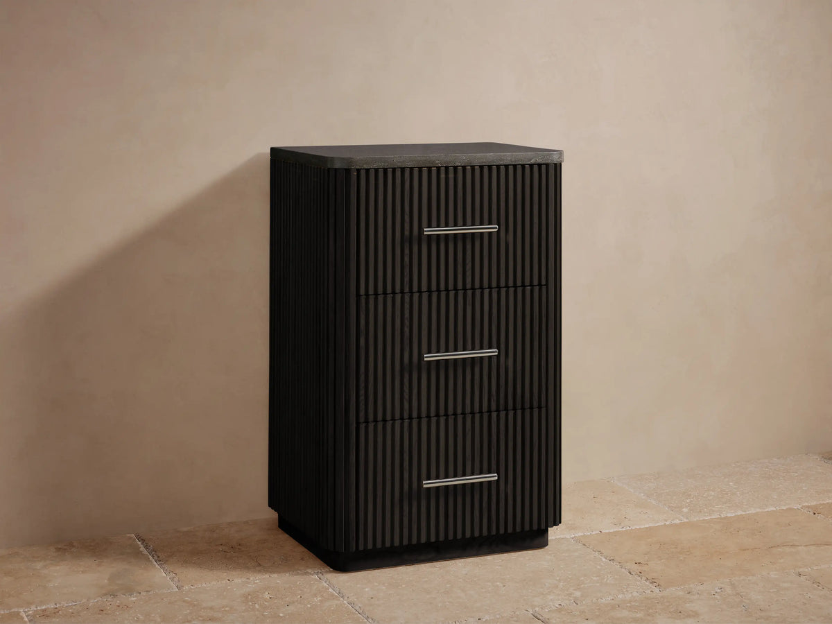 Close-up of Finnley Short Bath Cabinet's dark gray stone top with rounded corner over dark brown ribbed wood and silver handle.