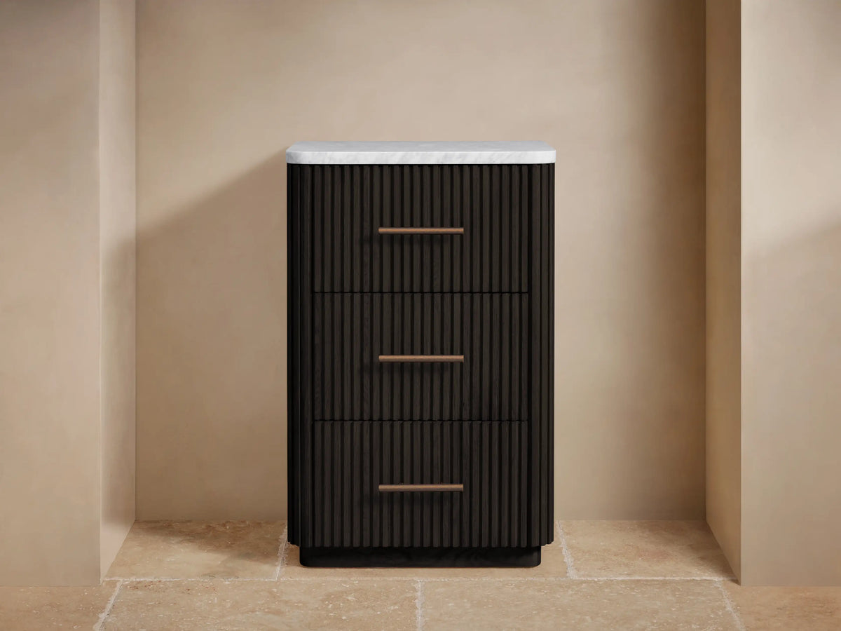 Dark brown Finnley Short Bath Cabinet with ribbed drawers, antique brass handles, and white marble top, styled with towels & flowers.