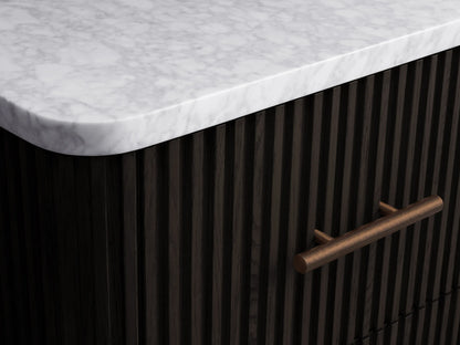 Finnley Short Bath Cabinet. Dark ribbed cabinet with white marble top, 3 drawers, antique brass pulls, on stone floor.