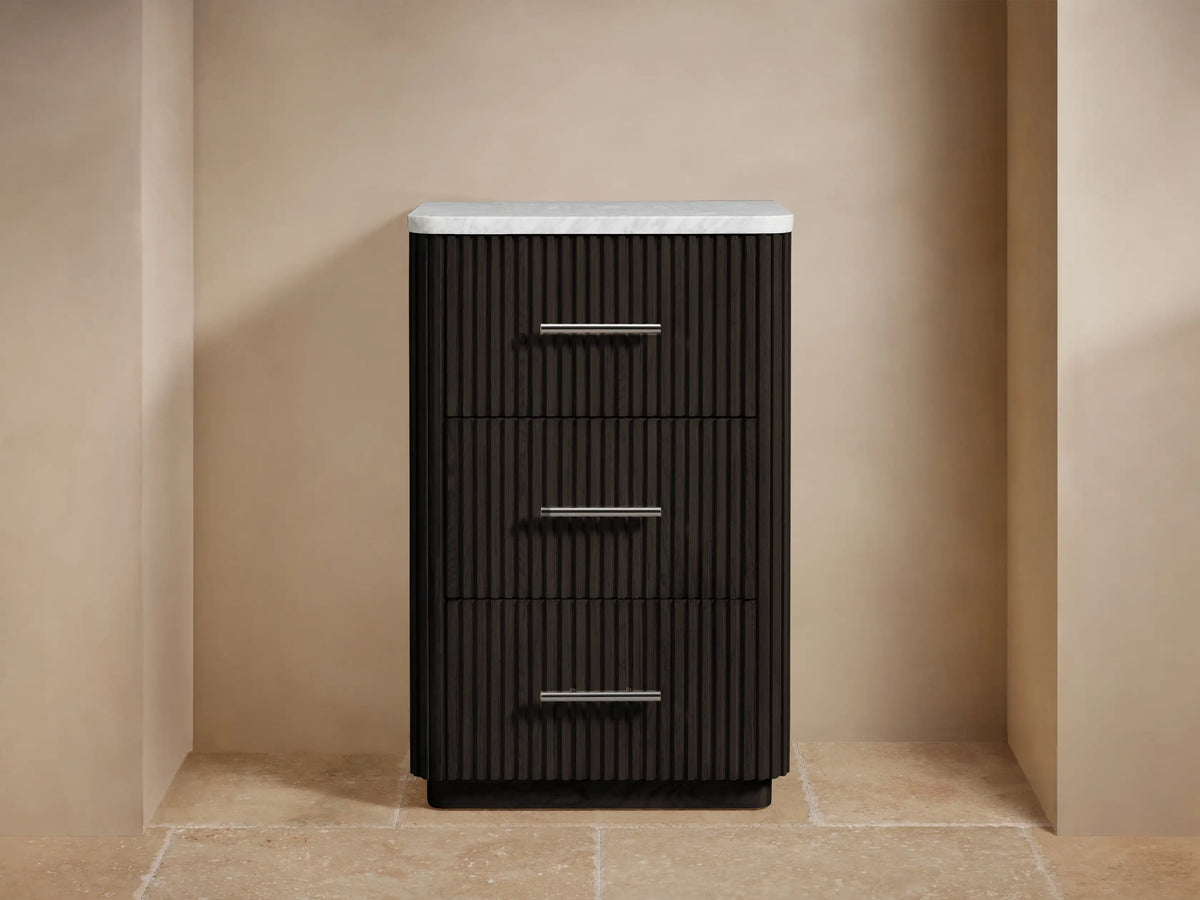 Dark brown Finnley Short Bath Cabinet with fluted fronts, white marble top, three drawers, and silver handles. Towels & flowers on top.