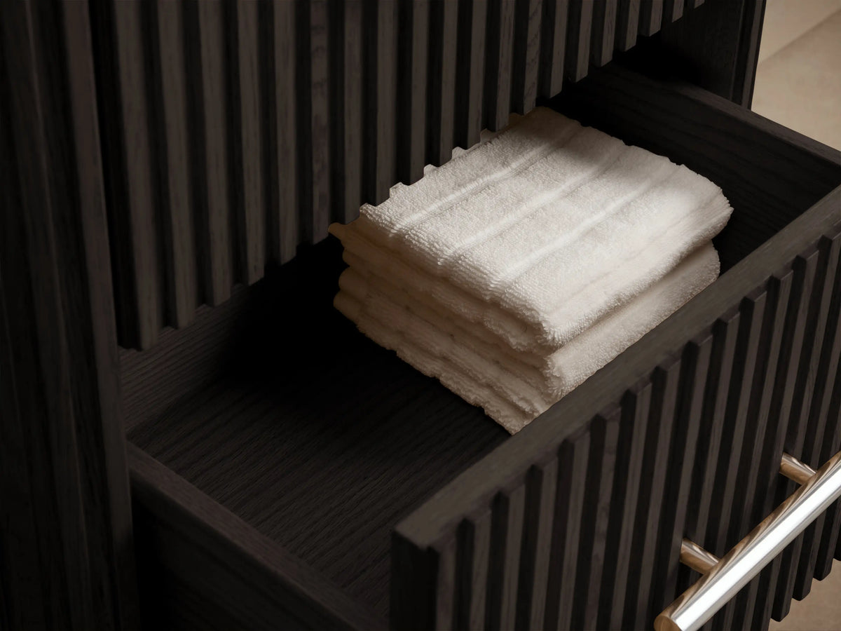 Finnley Short Bath Cabinet: dark fluted wood, 3 drawers with polished nickel pulls, white marble top, against beige wall.