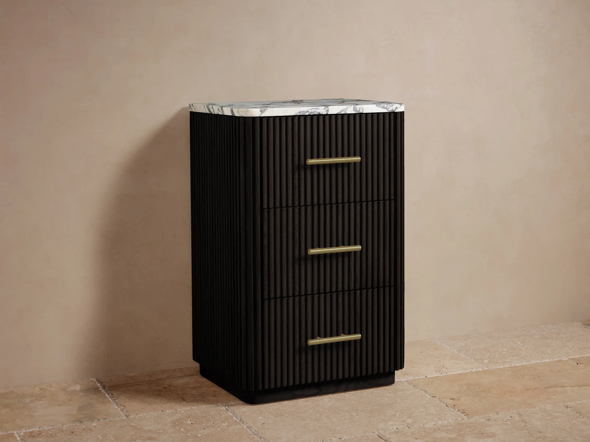 Finnley Short Bath Cabinet. Dark fluted cabinet with 3 brass pulls, white Carrara marble top. Towels and flowers on top.
