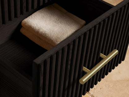 Finnley Short Bath Cabinet: dark, fluted wood cabinet with three drawers, brass pulls, and a white marble top, against a beige wall.