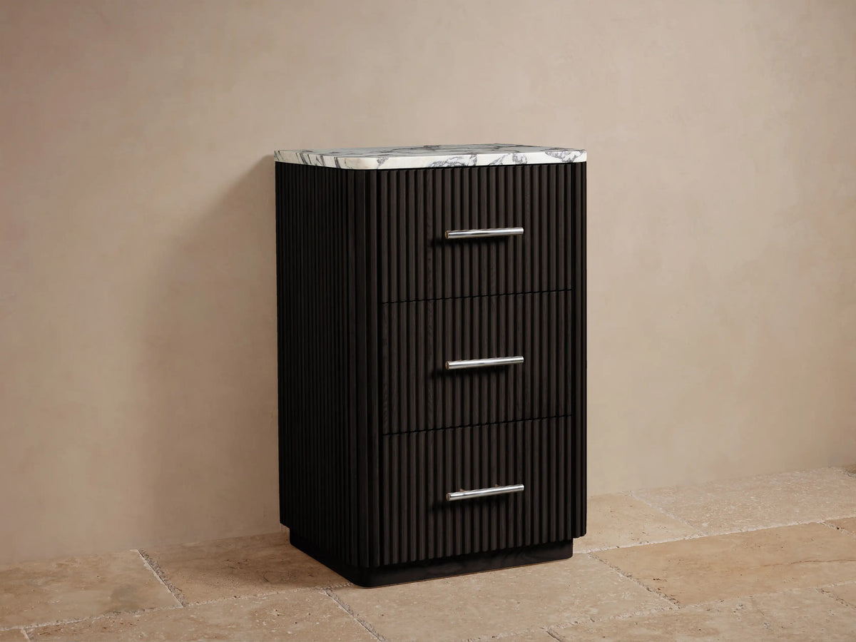 Angled close-up of Finnley Short Bath Cabinet. Honed white marble top with dark veining on dark fluted wood body with polished nickel handle.